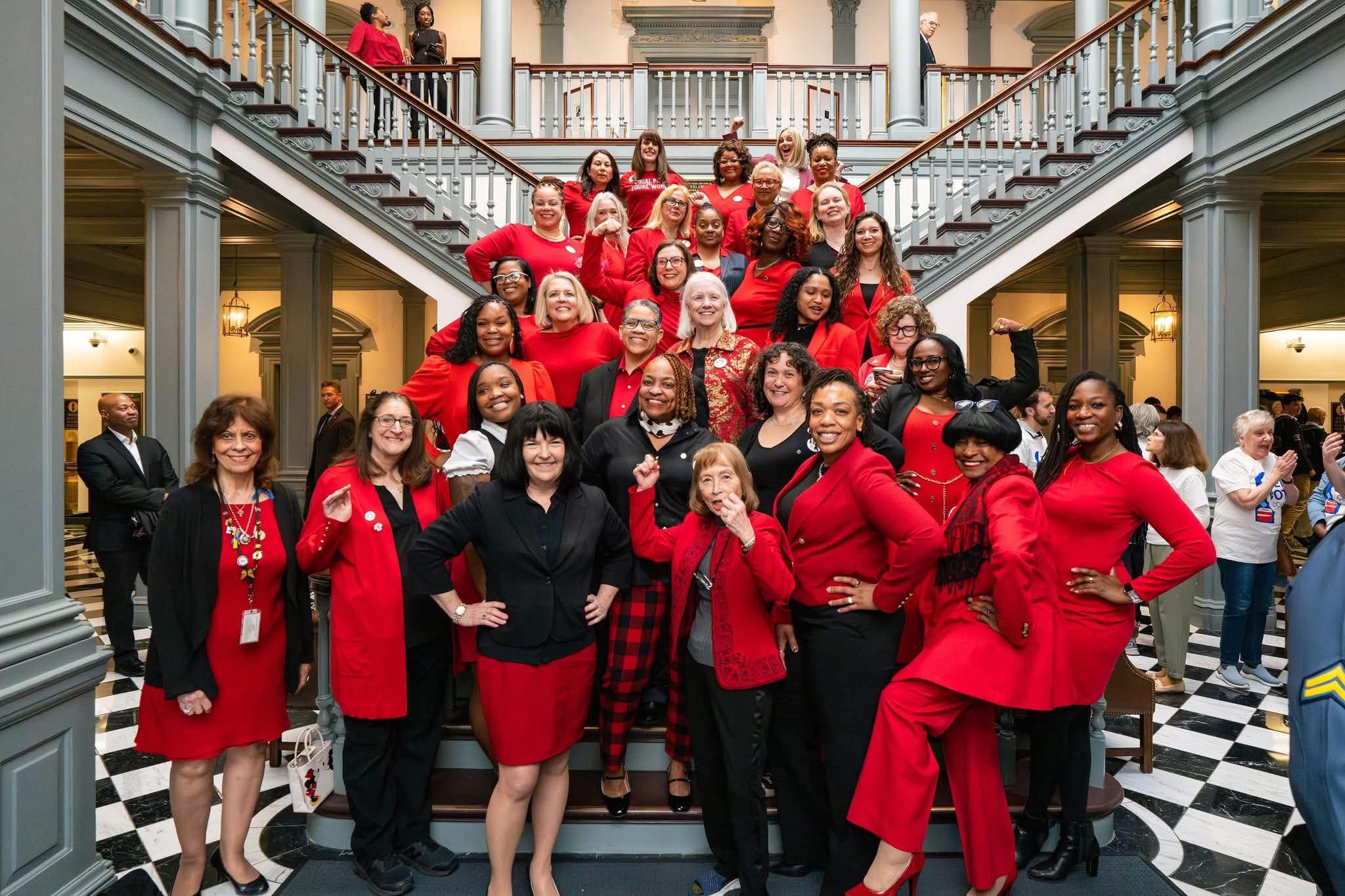 Group of all the women dressed in red for Equity day on the staircase in Legislative Hall.