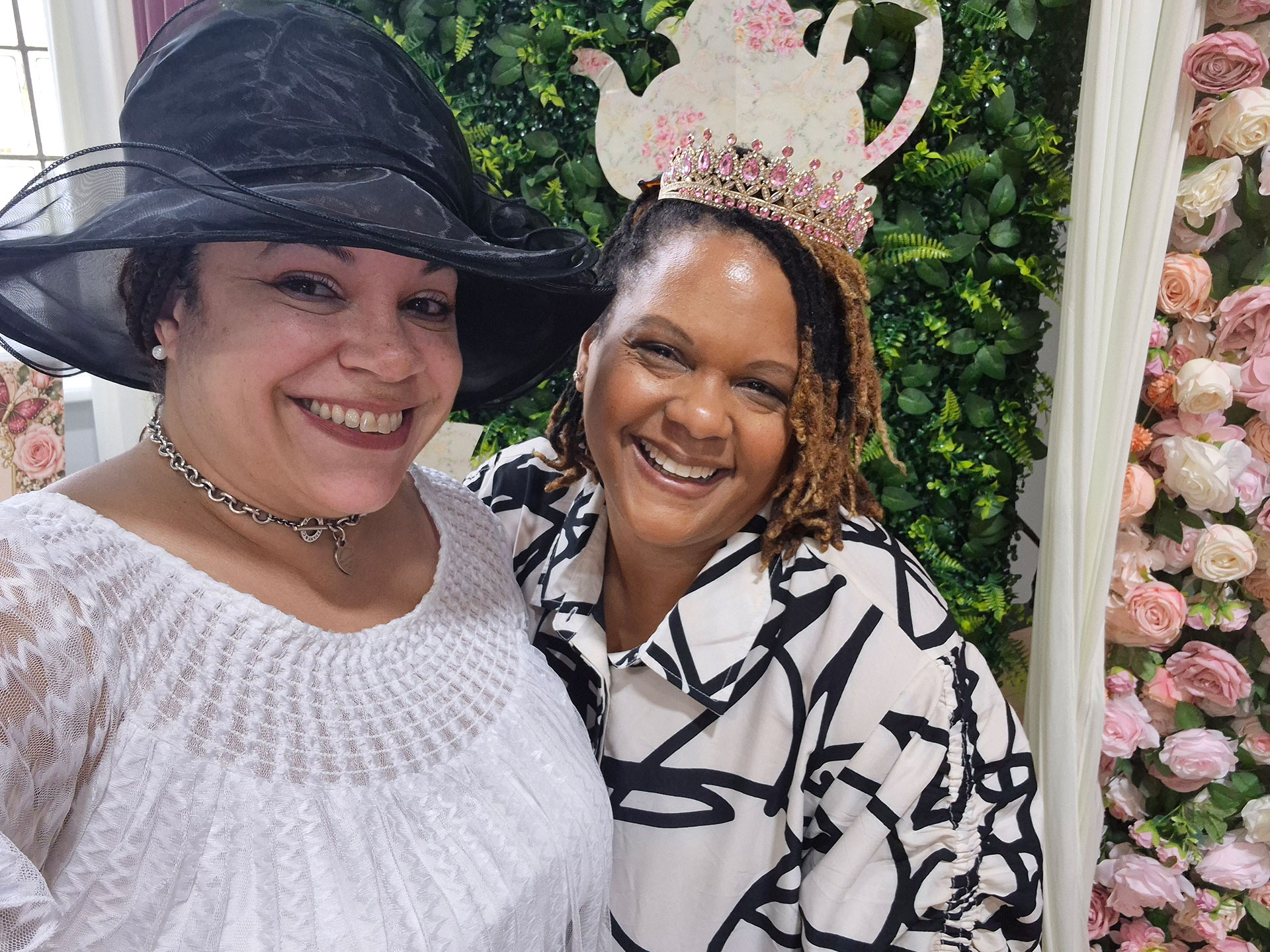 Two women at the I am My Sister's Keeper event. One wearing a white dress and a black hat. The other is wearing black and white dress with a crown.
